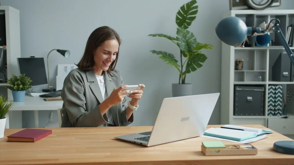 A woman in a home office using a smartphone while working on a laptop.