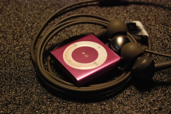 Close-up of a pink MP3 player with earphones coiled around it on a textured surface.