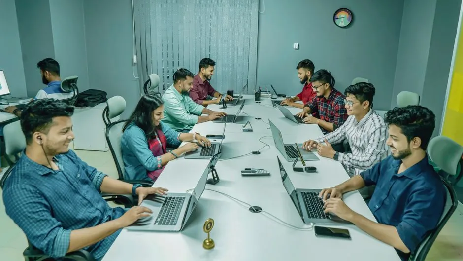 Group of professionals collaborating in a modern office setting on laptops and digital devices.