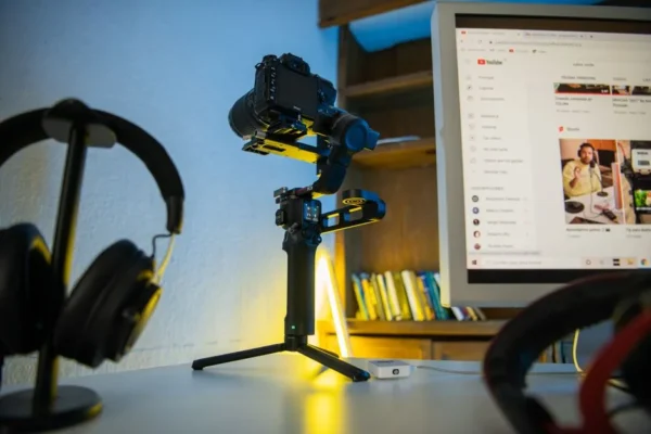 Professional photography setup featuring a camera on a tripod, headphones, and a computer monitor displaying video content.