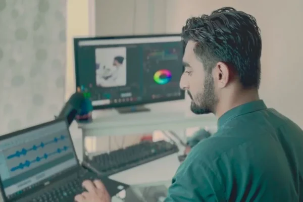 Man working in office on editing software with dual displays, laptop, and professional setup