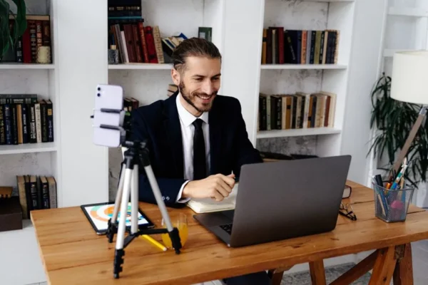 Businessman in suit smiling during a video call from his home office, sitting at a wooden desk.